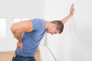 Young Man Having Backache While Leaning On White Wall